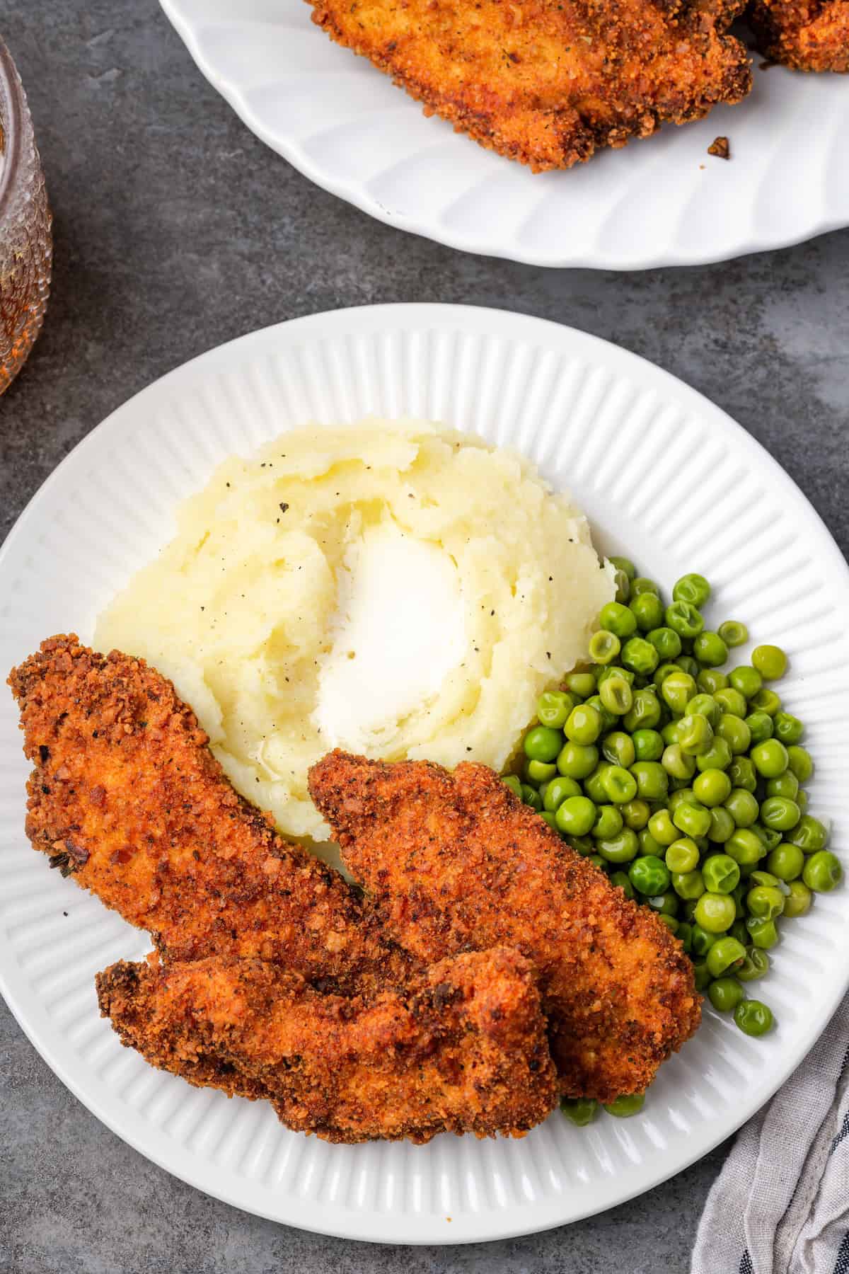 Overhead view of crispy chicken tenders breaded with chicken stuffing next to mashed potatoes and peas on a plate.