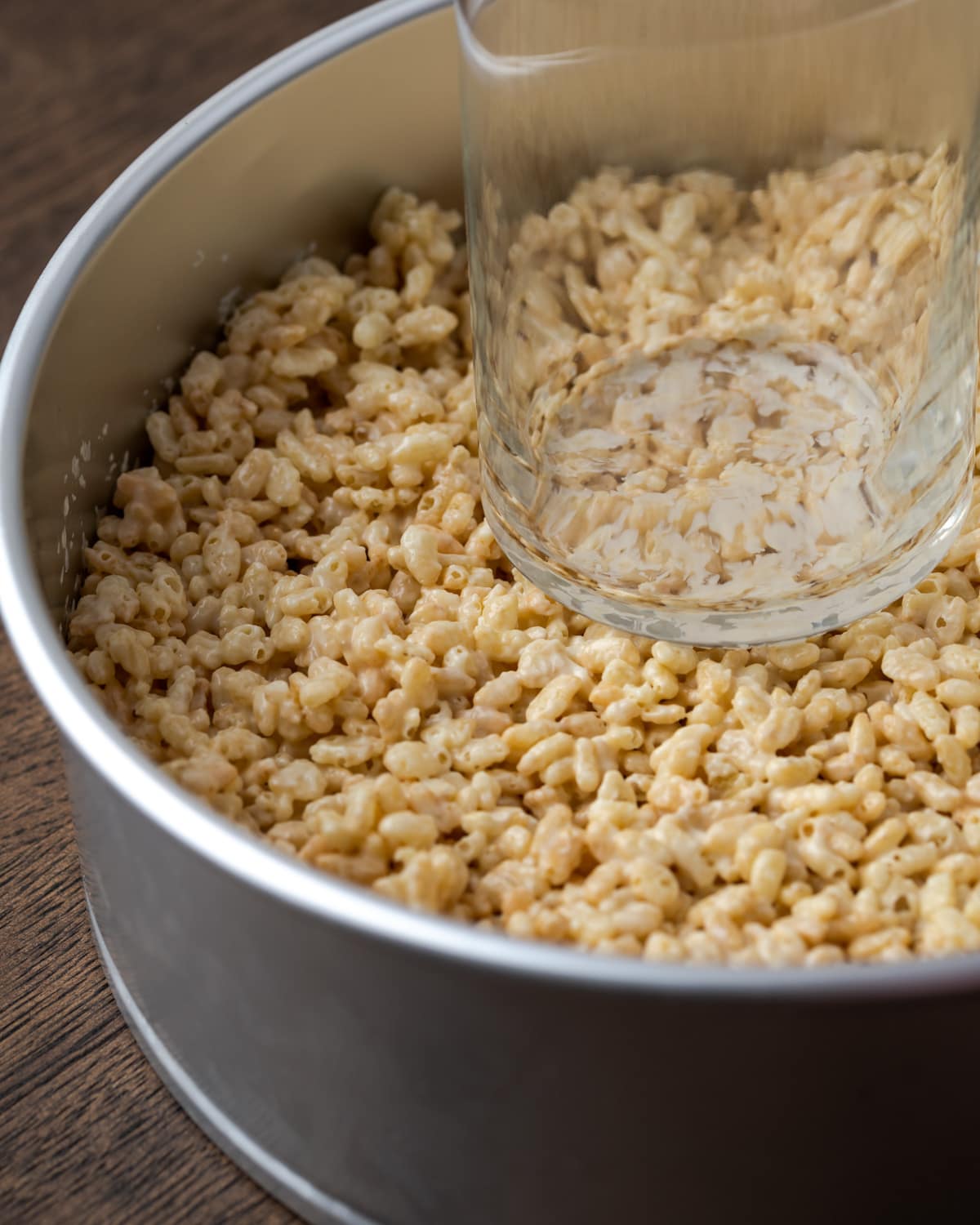 The bottom of a glass is used to press the Rice Krispie treat layer into the bottom of a springform pan.