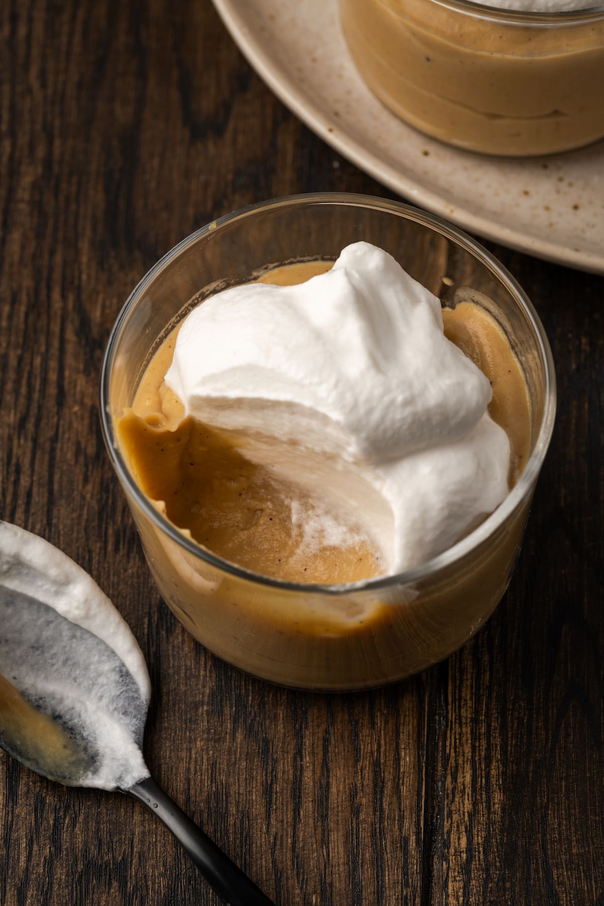 Butterscotch pudding topped with whipped cream in a glass, with a spoonful missing.