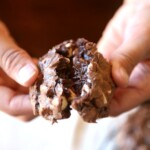 Two hands pull apart a chocolate brownie cookie to reveal the fudgy interior.