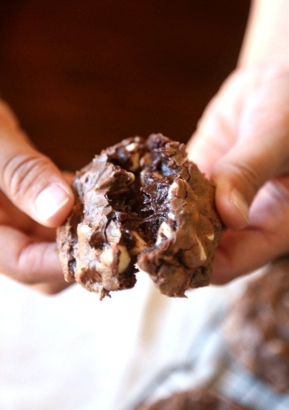 Two hands pull apart a chocolate brownie cookie to reveal the fudgy interior.