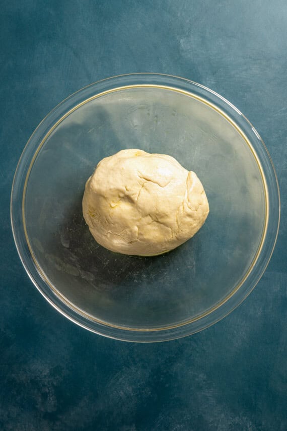 A ball of pretzel dough in a glass bowl.