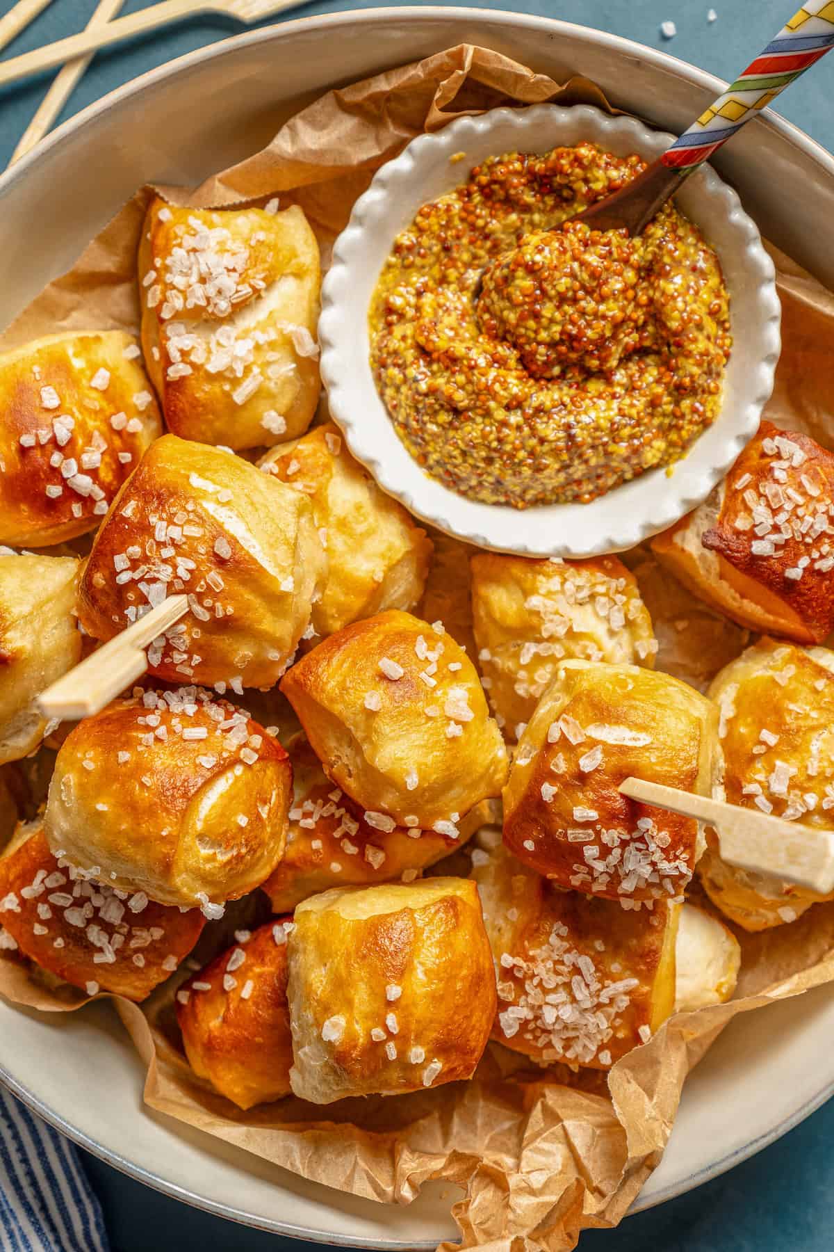 Overhead view of soft pretzel bites arranged on a plate next to a bowl of whole grain mustard for dipping.
