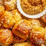 Close up overhead view of soft pretzel bites piled on a plate next to a bowl of whole grain mustard for dipping.