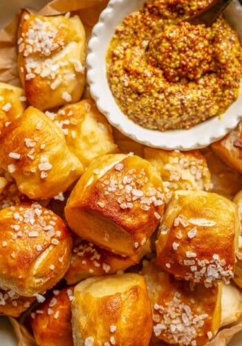Close up overhead view of soft pretzel bites piled on a plate next to a bowl of whole grain mustard for dipping.