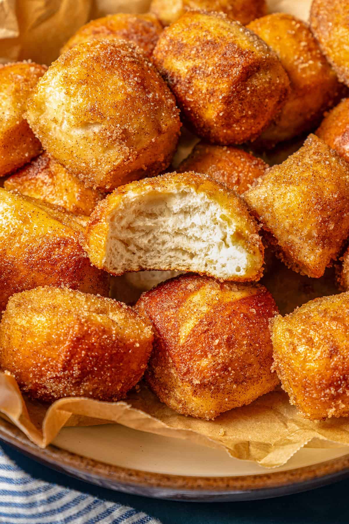 Close up view of cinnamon sugar soft pretzel bites inside a parchment-lined bowl, with a bite missing from one of the nuggets.