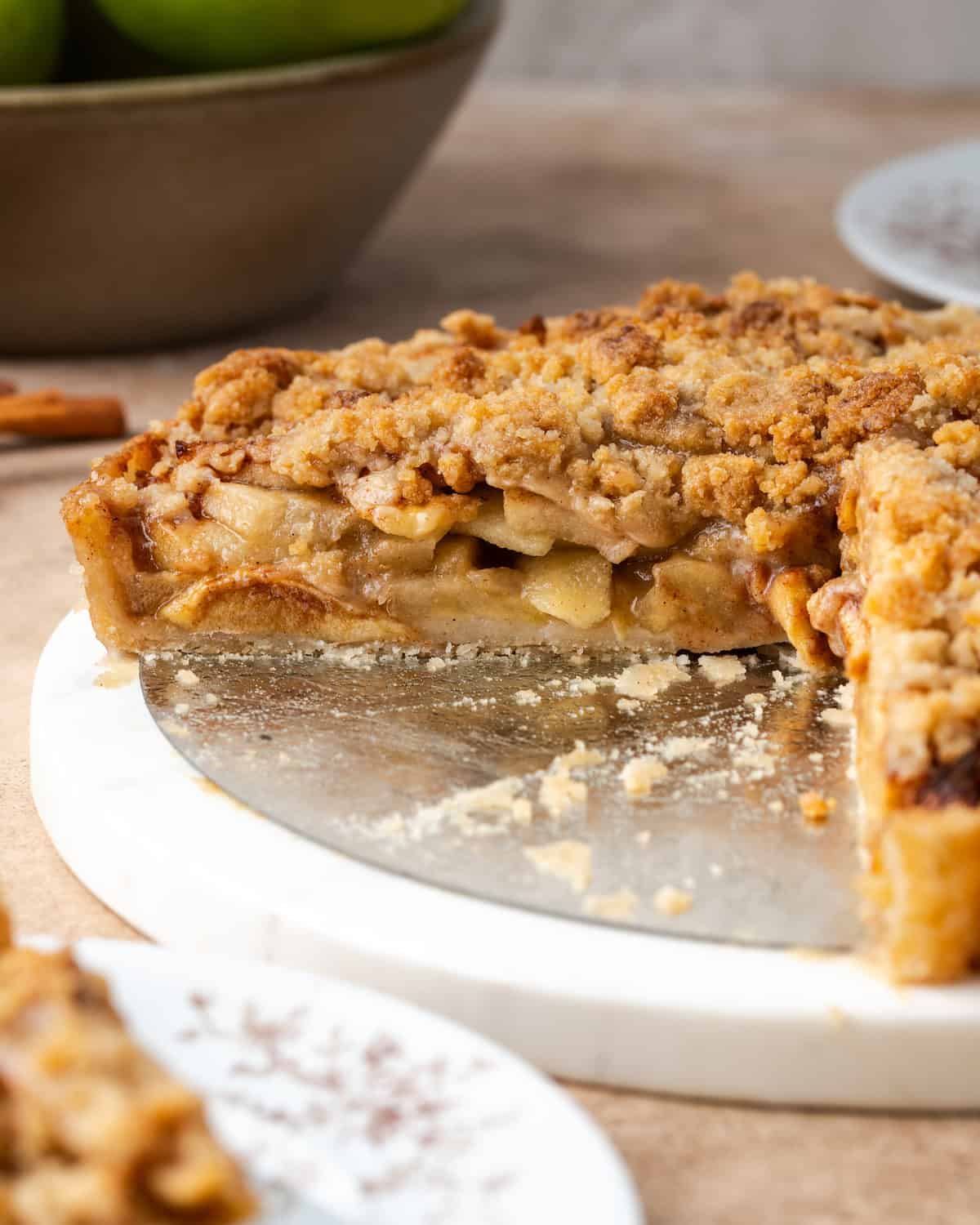 Side view of an apple crumble tart with a large slice missing.