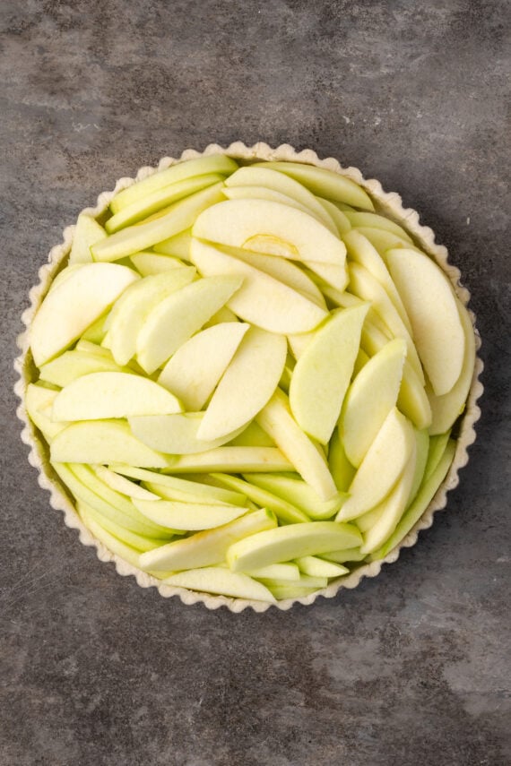 Apple slices piled into a pie crust in a tart pan.