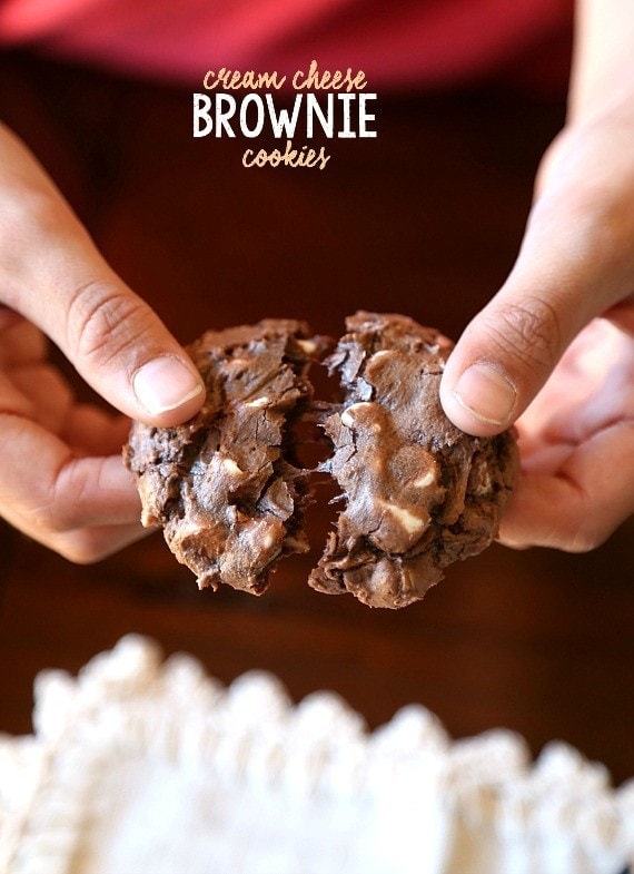 Two hands pull apart a chocolate brownie cookie to reveal the fudgy interior.