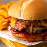 Candied bacon maple cheddar burger on a wooden board next to curly fries.