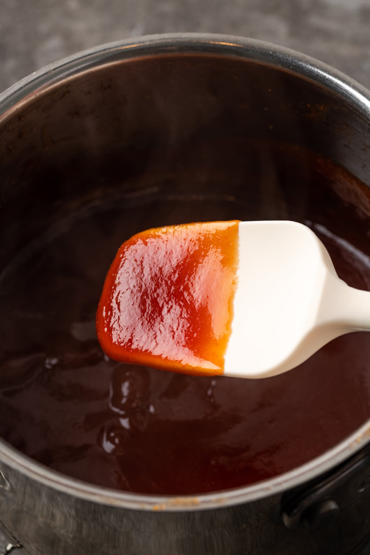 A spatula dipped in maple BBQ sauce held over a pot of simmering sauce.