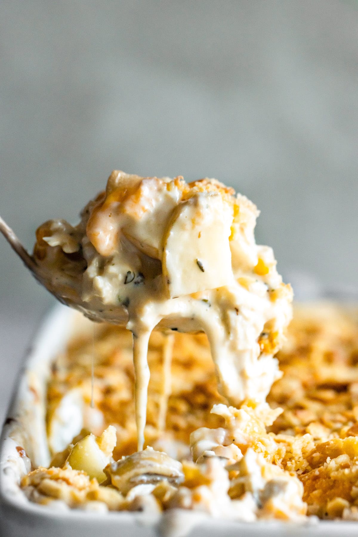 A spoon lifting a serving of cheesy chicken hashbrown casserole from a baking dish.