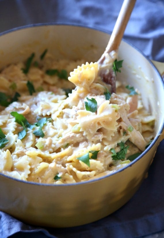 Cheesy chicken and bow tie pasta in a large pot with a serving spoon.