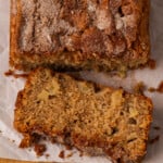 Overhead view of a loaf of apple cinnamon bread with a slice cut from the end on a wooden cutting board.