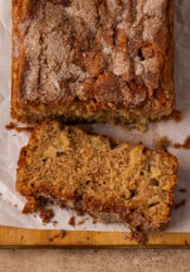 Overhead view of a loaf of apple cinnamon bread with a slice cut from the end on a wooden cutting board.