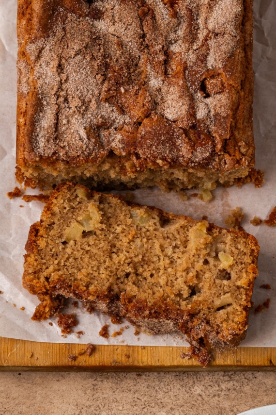 Overhead view of a loaf of apple cinnamon bread with a slice cut from the end on a wooden cutting board.