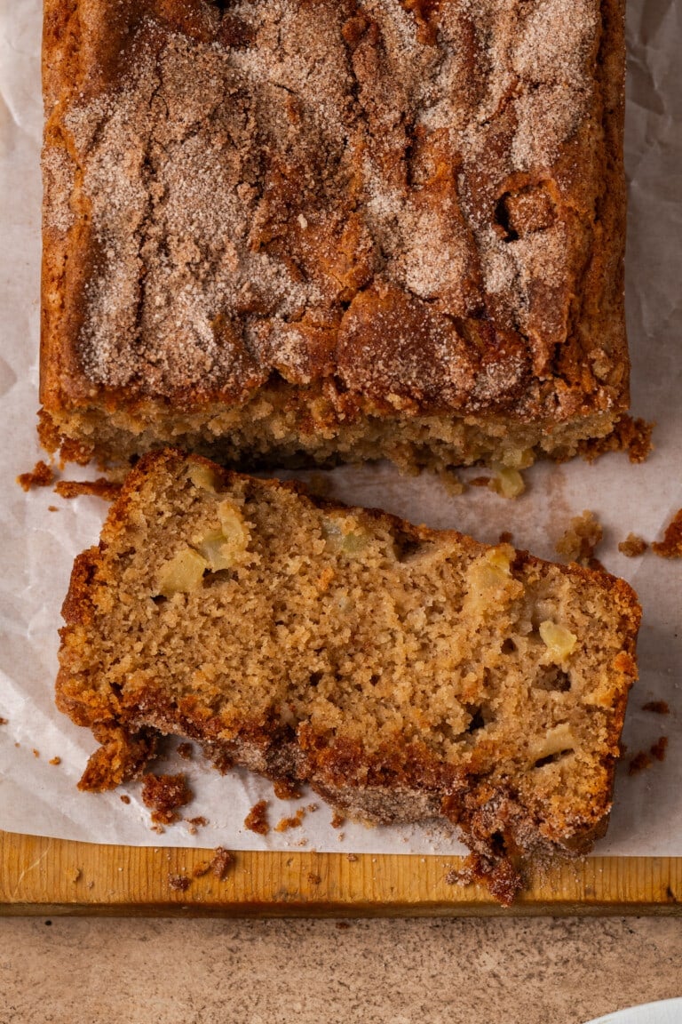 Overhead view of apple cinnamon bread with a slice cut from the edge on a wooden cutting board.