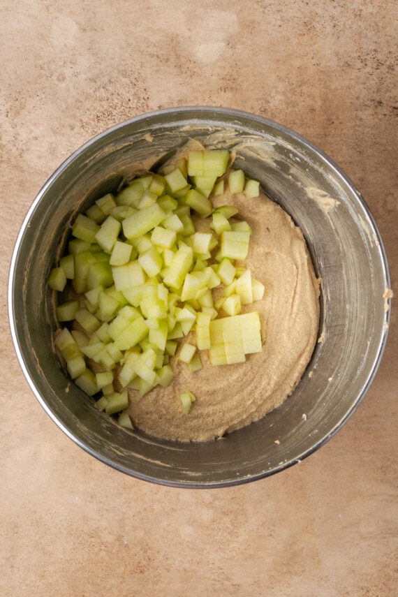 Chopped apples added to cinnamon bread batter in a mixing bowl.