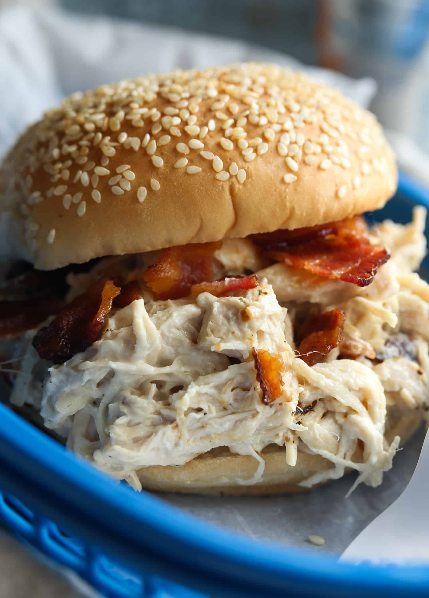 Slow cooker crack chicken served in a bun topped with bacon on a blue plate.