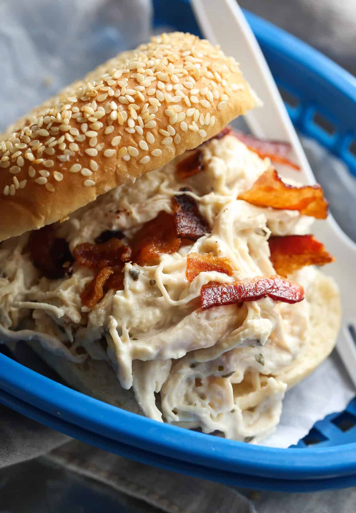 Slow cooker crack chicken served in a bun topped with bacon on a blue plate.