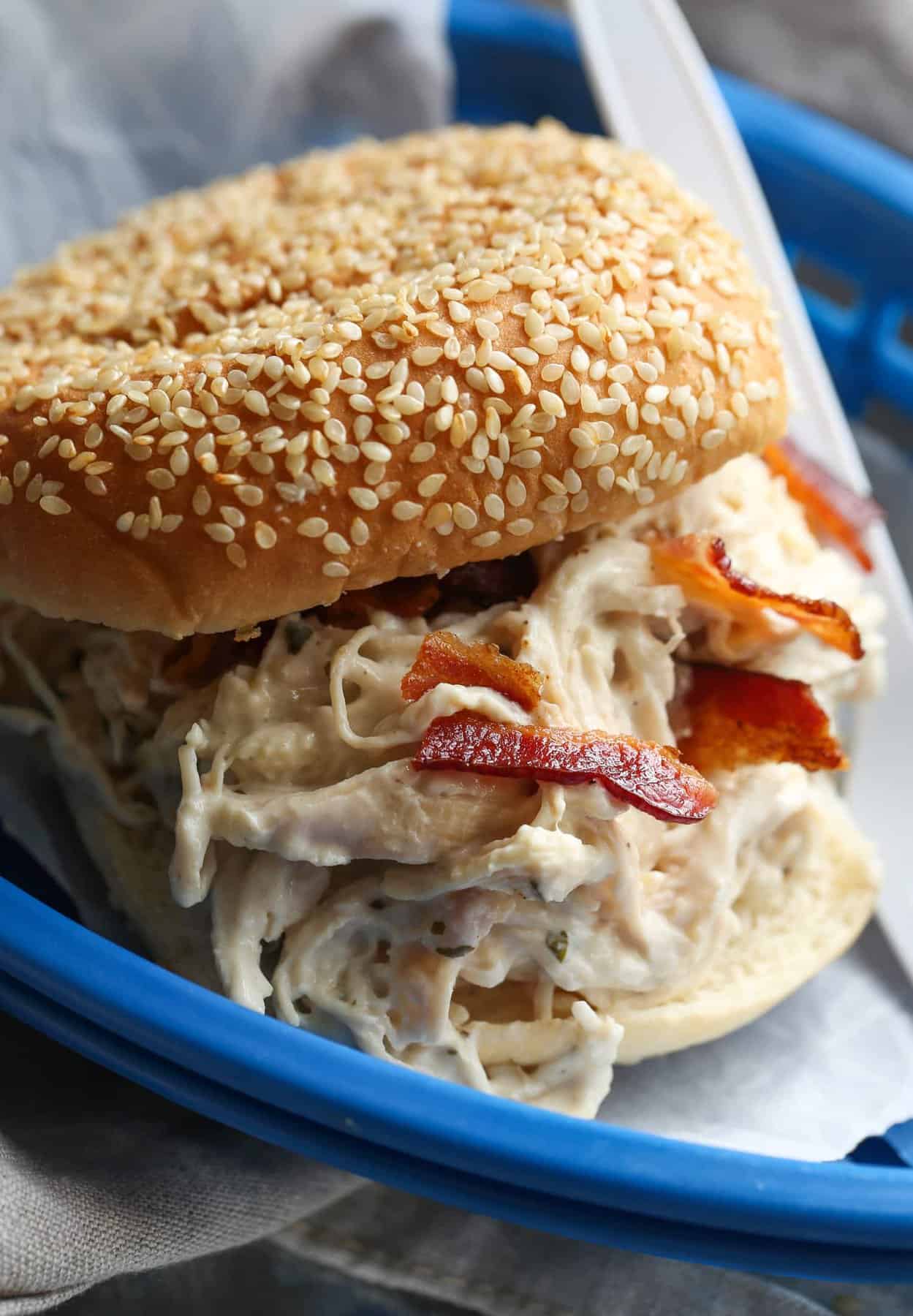 Slow cooker crack chicken served in a bun topped with bacon on a blue plate.