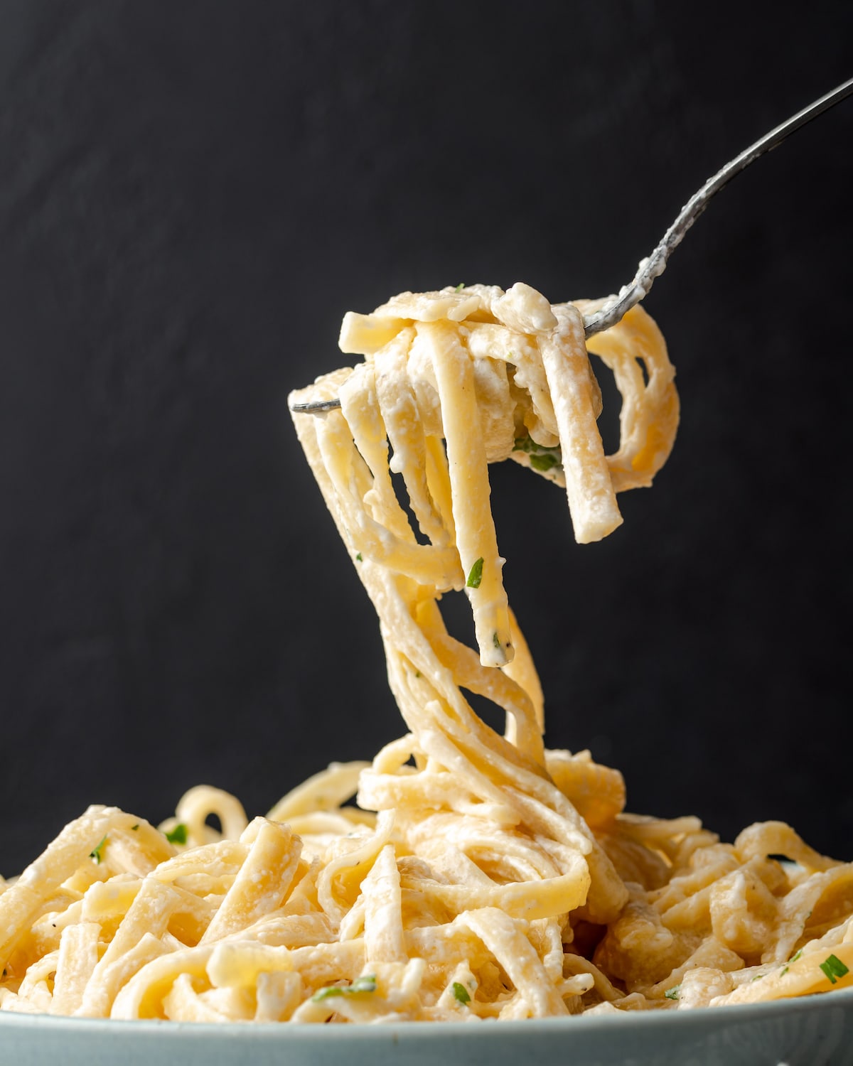A forkful of fettuccine Alfredo pasta over a bowl of pasta noodles.