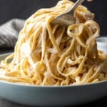Fettuccine pasta is tossed in homemade Alfredo sauce in a large bowl.