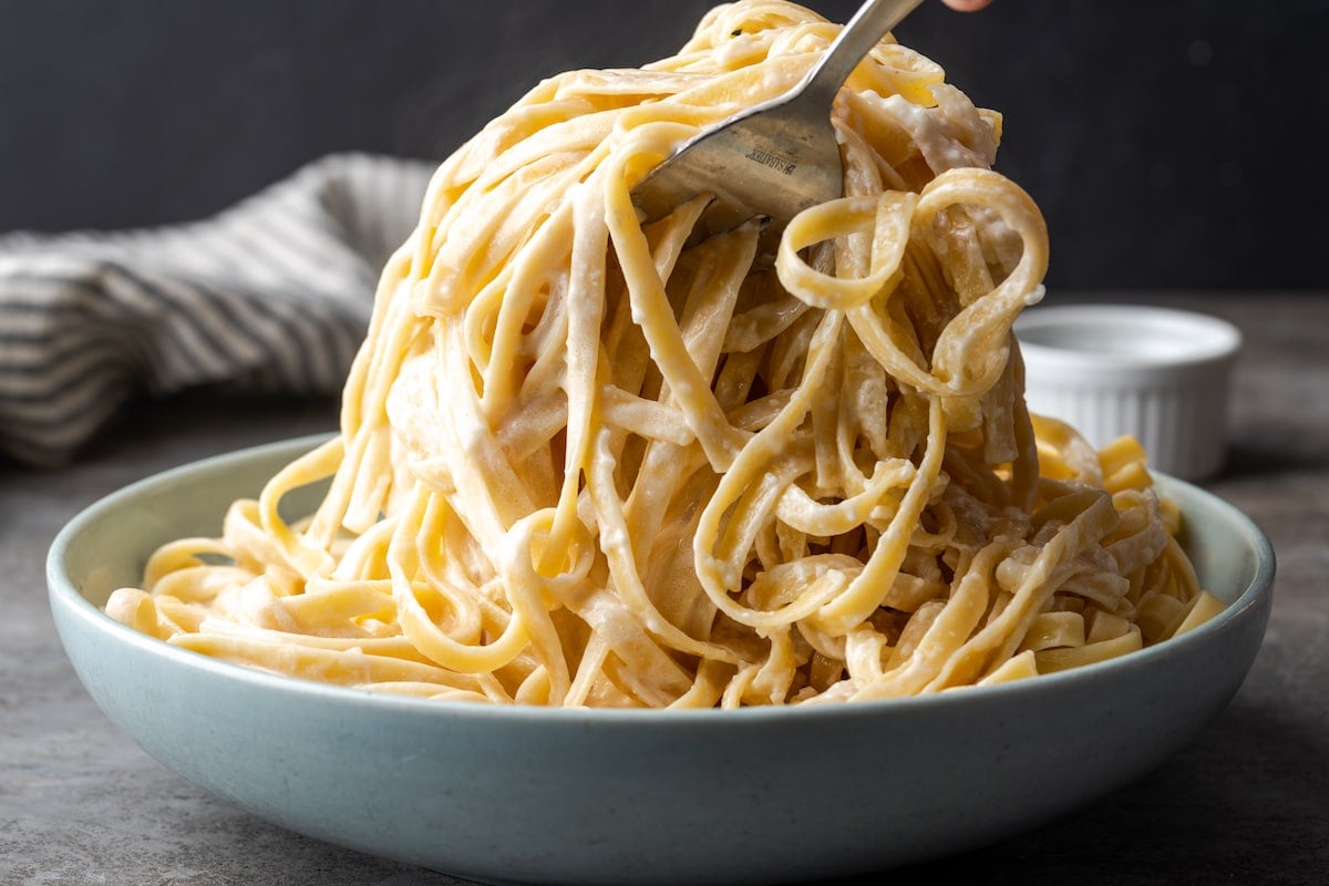 Fettuccine pasta is tossed in homemade Alfredo sauce in a large bowl.