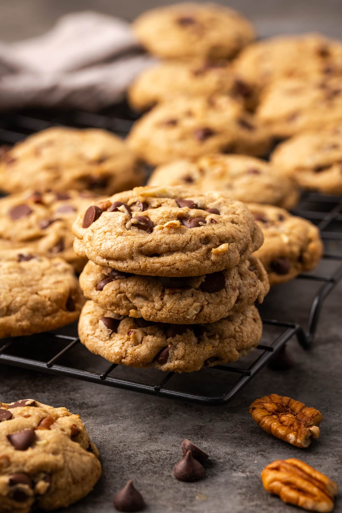 A stack of browned butter bourbon chocolate chip cookies on the corner of a wire rack, with more cookies in the background.