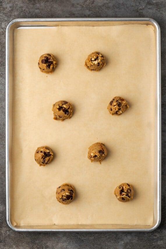 Chocolate chip cookie dough balls on a parchment-lined baking sheet.