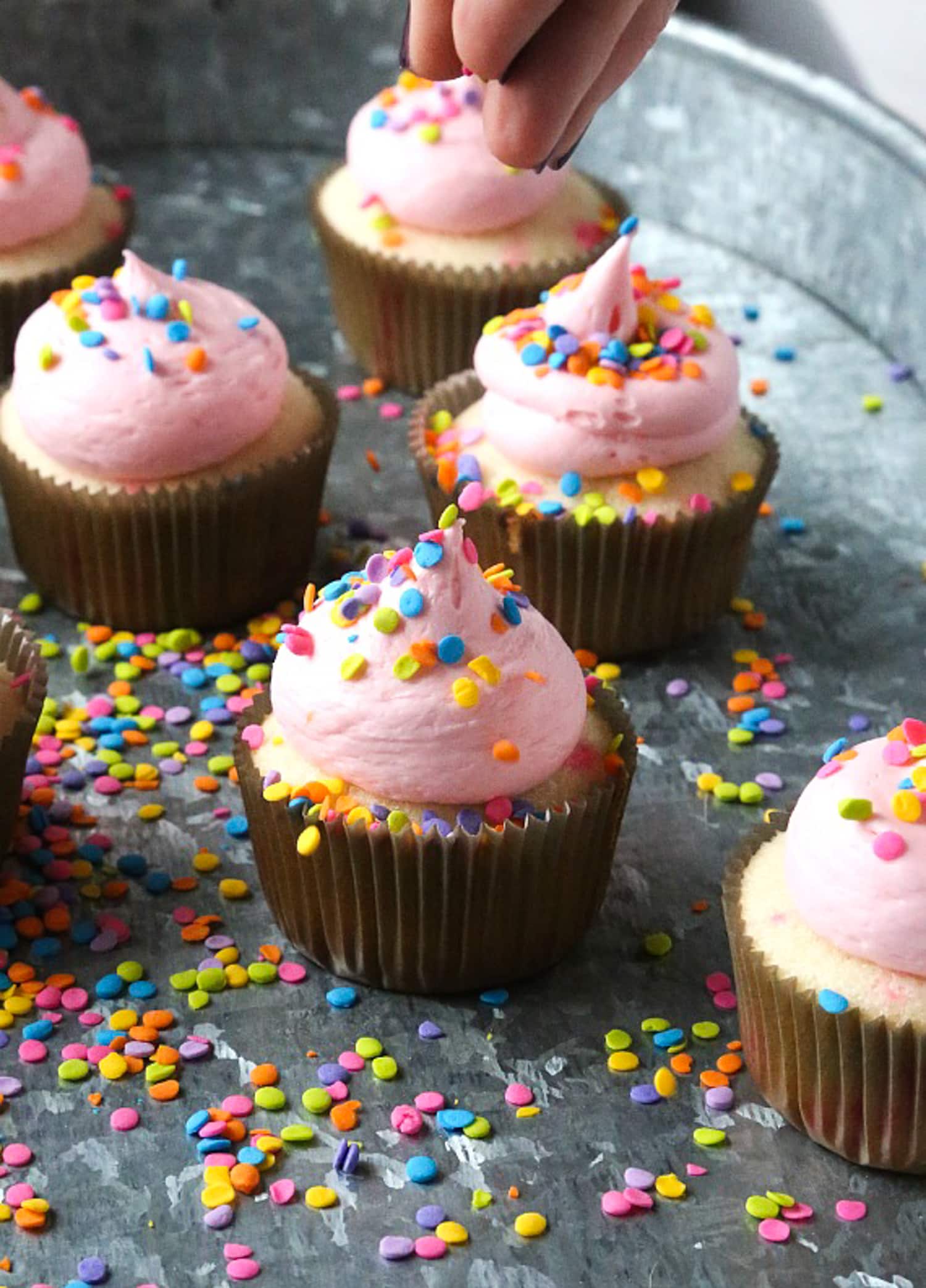 tossing sprinkles into a funfetti sprinkle cupckae with pink buttercream