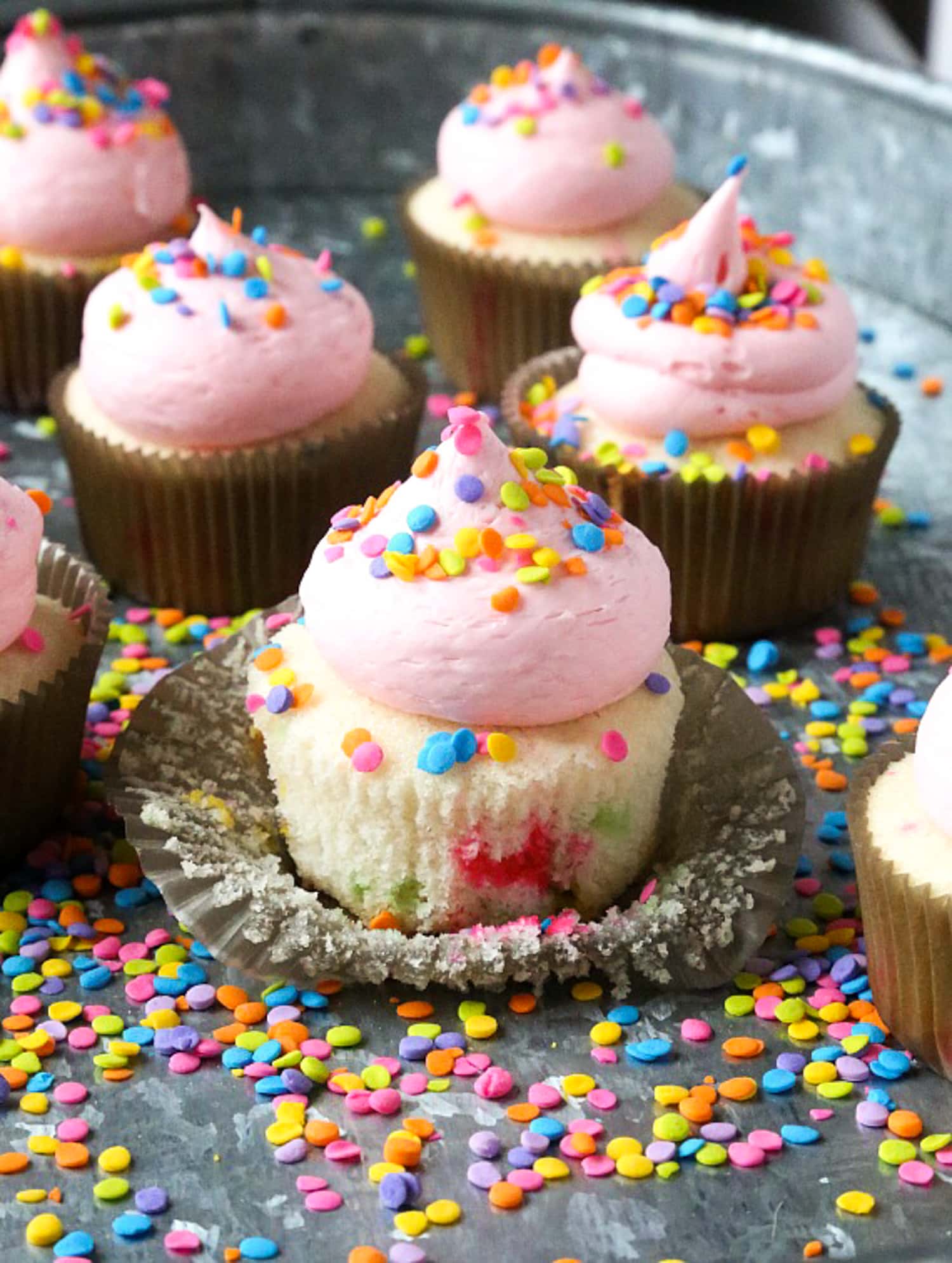 A streusel cupcake with peeled foil topped with pink buttercream frosting and sprinkles