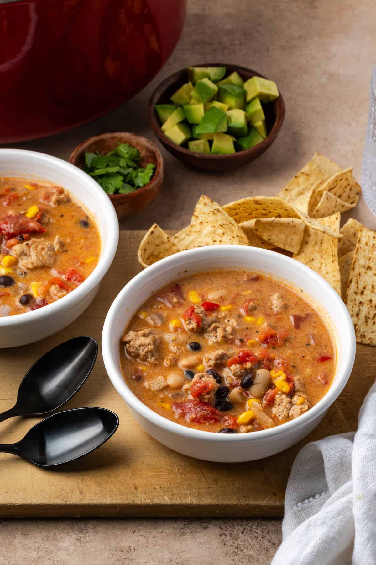 Two bowls of creamy taco soup on a wooden board next to two spoons.