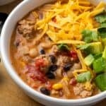 A bowl of creamy taco soup topped with shredded cheese and diced avocado.