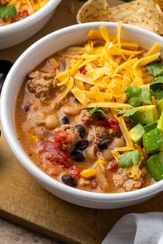 A bowl of creamy taco soup topped with shredded cheese and diced avocado.
