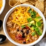 Overhead view of a bowl of creamy taco soup topped with shredded cheese and diced avocado.