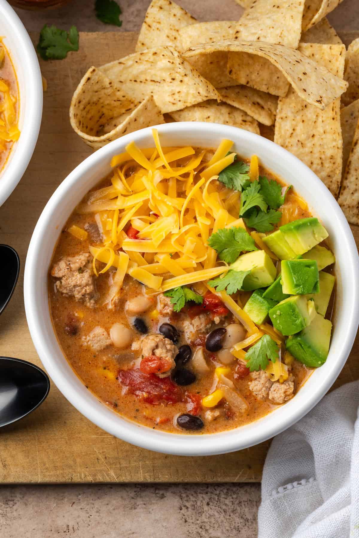 Overhead view of a bowl of creamy taco soup topped with shredded cheese and diced avocado.