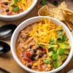 Overhead view of two bowls of creamy taco soup topped with shredded cheese and diced avocado.