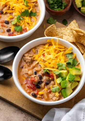 Overhead view of two bowls of creamy taco soup topped with shredded cheese and diced avocado.
