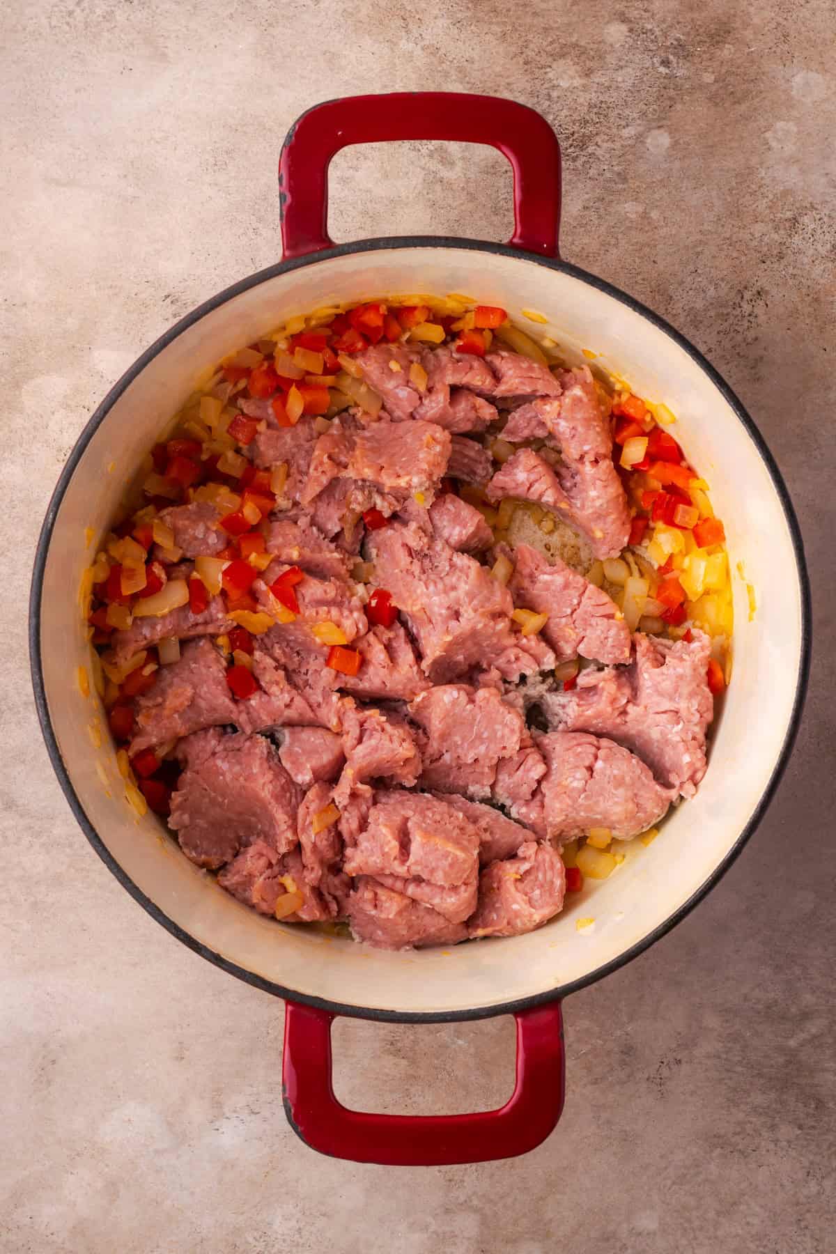 Ground beef added to sautéed veggies in a pot.