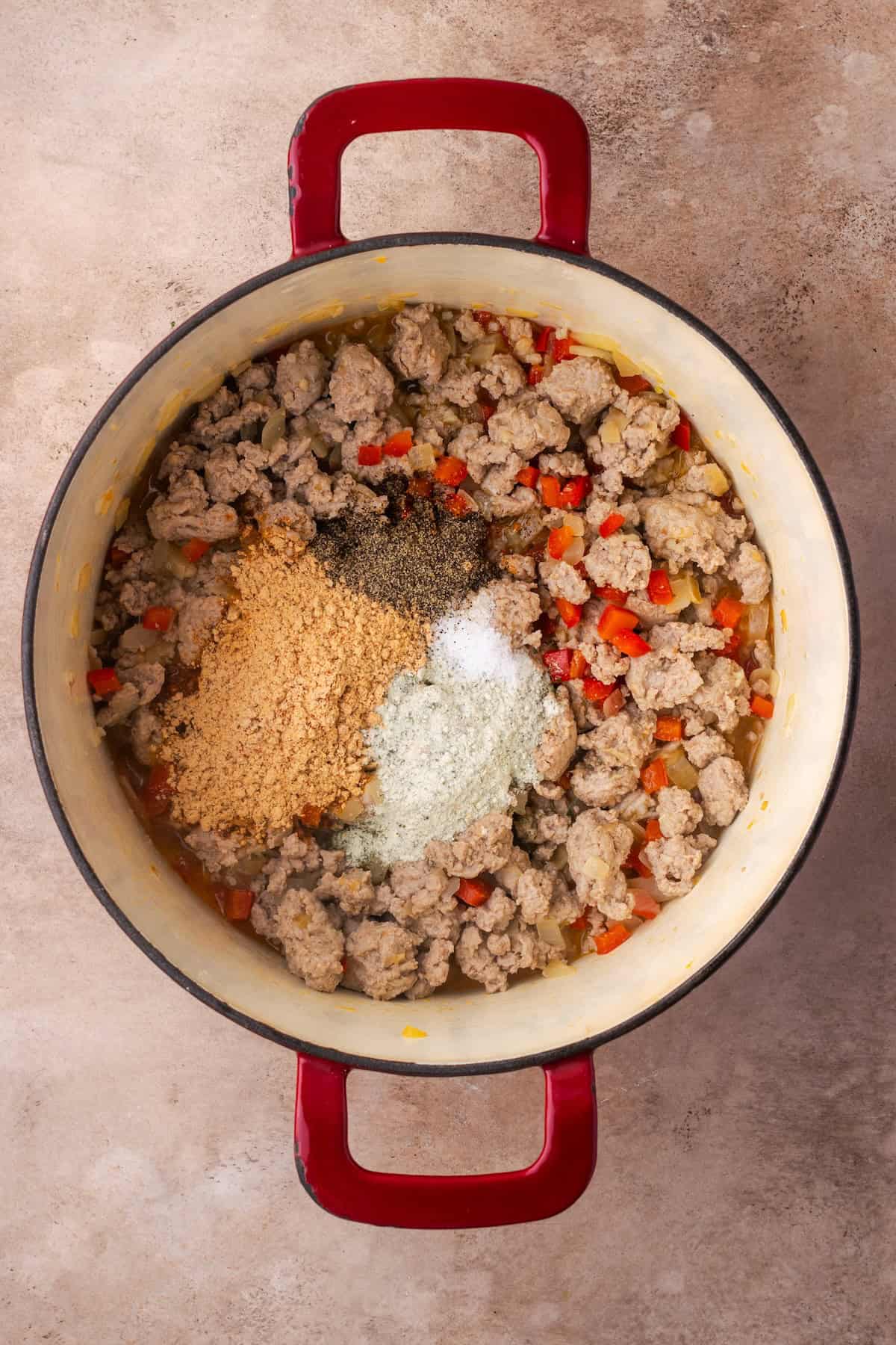 Seasonings added to browned ground meat and veggies in a pot.
