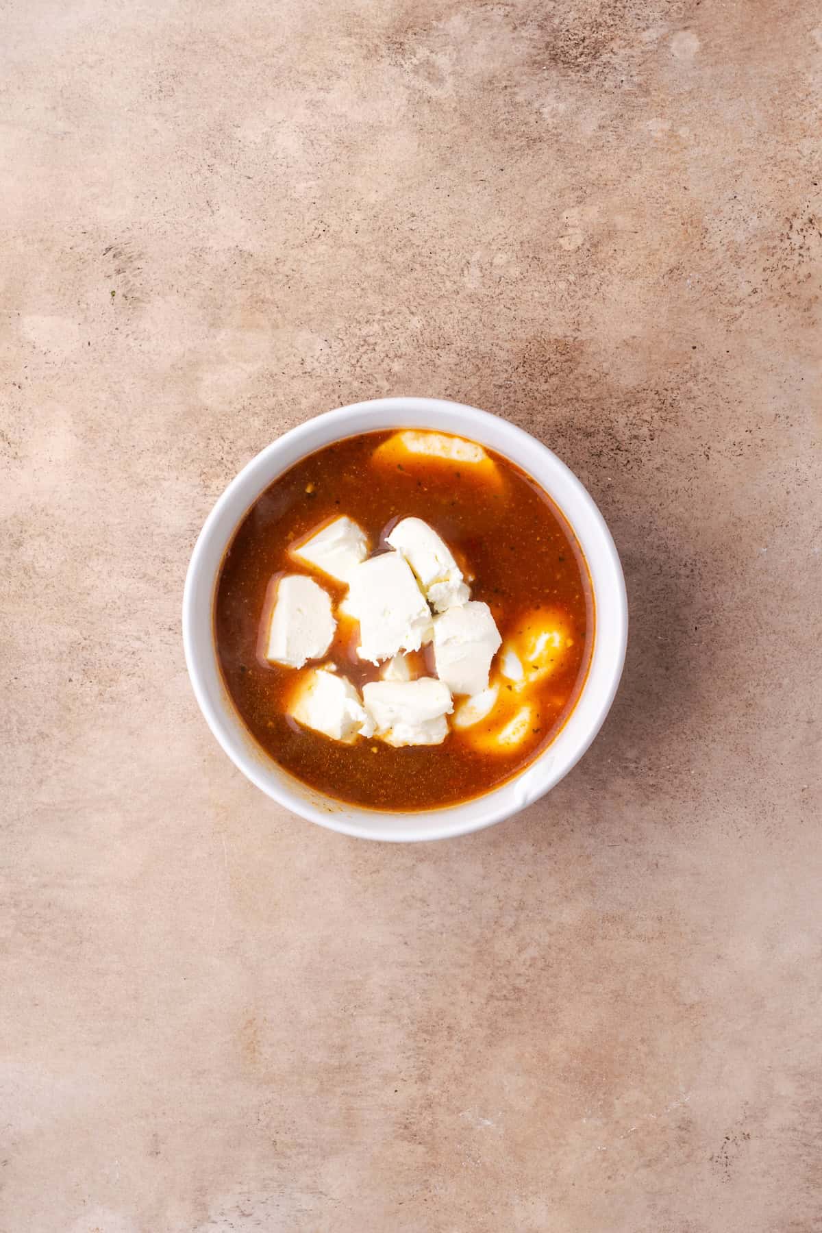 Soup broth added to a bowl with yogurt and cream cheese, to temper it.