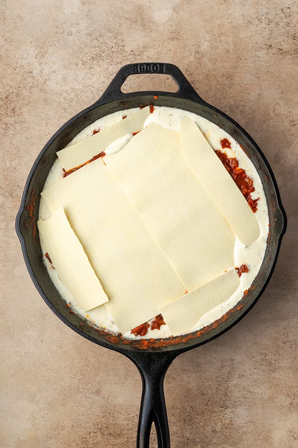 Lasagna noodles layered over meat sauce and cheese in a skillet.