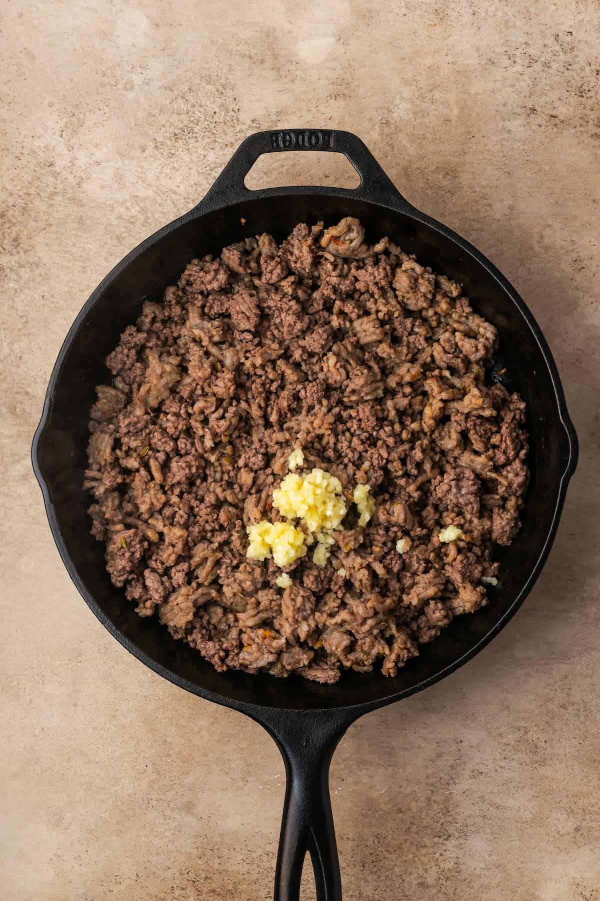 Garlic added to browned ground meat in a skillet.