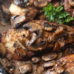 Chicken in a skillet topped with mushrooms and garlic