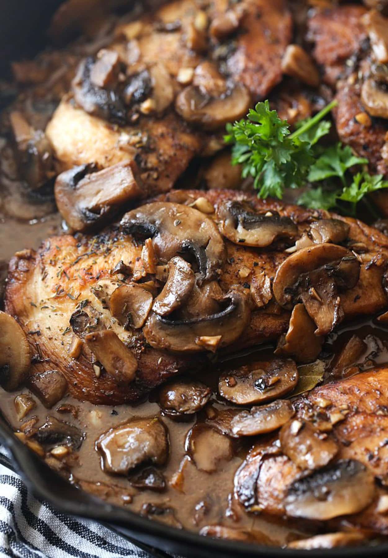 Chicken in a skillet topped with mushrooms and garlic