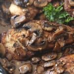 Chicken in a skillet topped with mushrooms and garlic