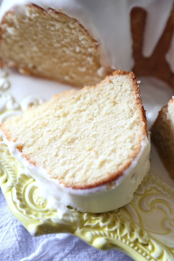 A thick slice of Meyer lemon bundt cake next to the rest of the cake.