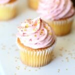 Assorted vanilla cupcakes topped with swirls of strawberry buttercream frosting.