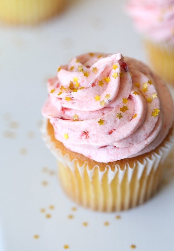 A vanilla cupcake topped with a swirl of strawberry buttercream frosting.